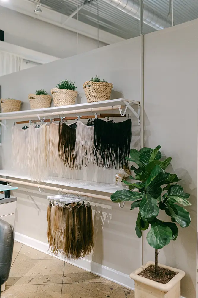 Shelves displaying various shades of hair extensions hang neatly below decorative baskets with plants; a potted plant sits on the tiled floor. - Chevalrie Salon and Spa